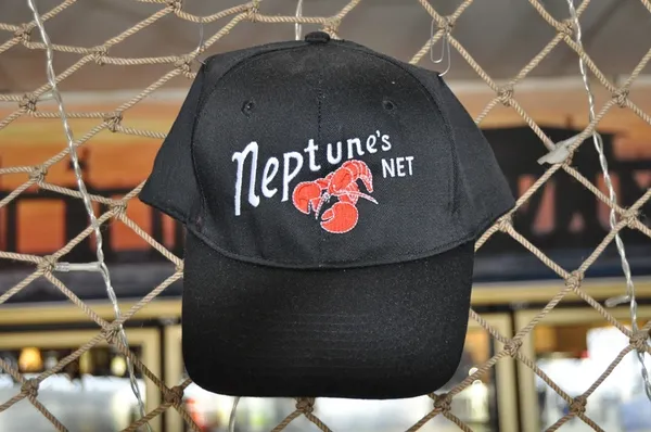 A black hat hanging on the fence of a cage.